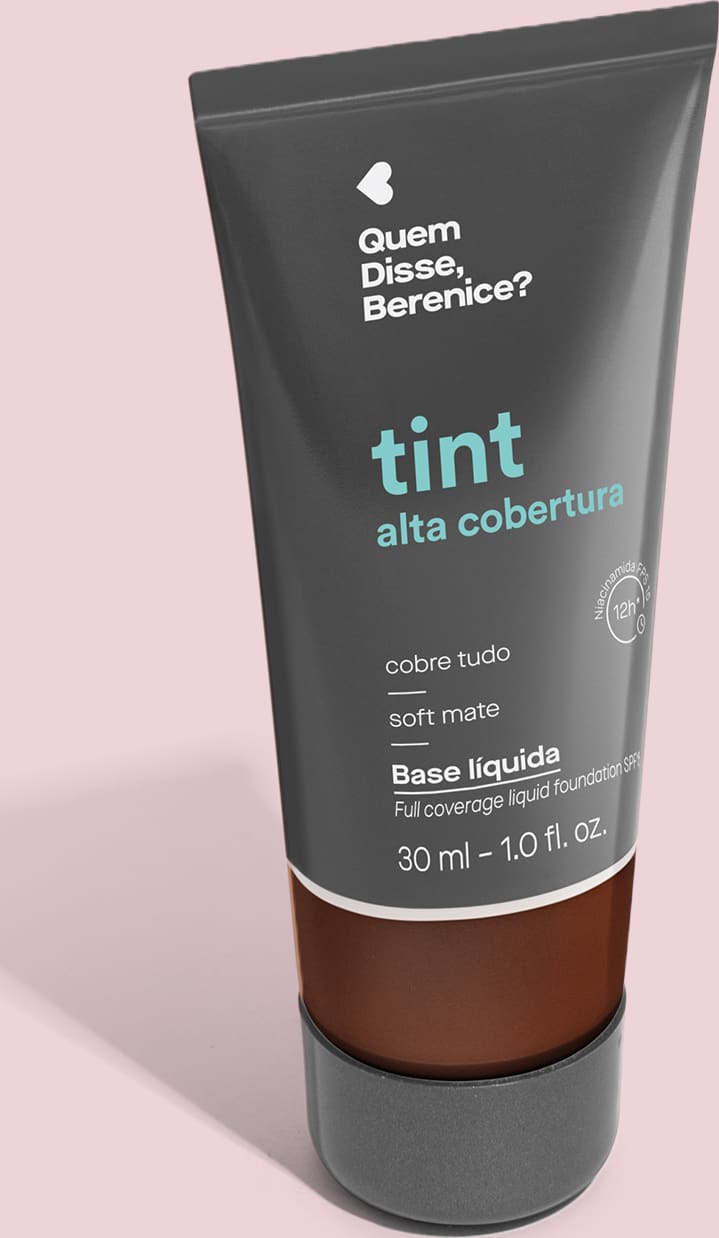 A imagem mostra a Base Tint Alta Cobertura da Quem Disse, Berenice? Embalagem preta com parte inferior transparente para mostrar a cor do produto sobre fundo rosa.