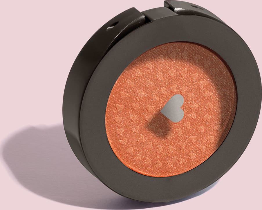 Estojo compacto redondo na cor preta com tampa transparente e coração ilustrado contendo 2g de blush em pó compacto Rubor Cobre Cobrelito da mara Quem Disse, Berenice? em fundo lilás.