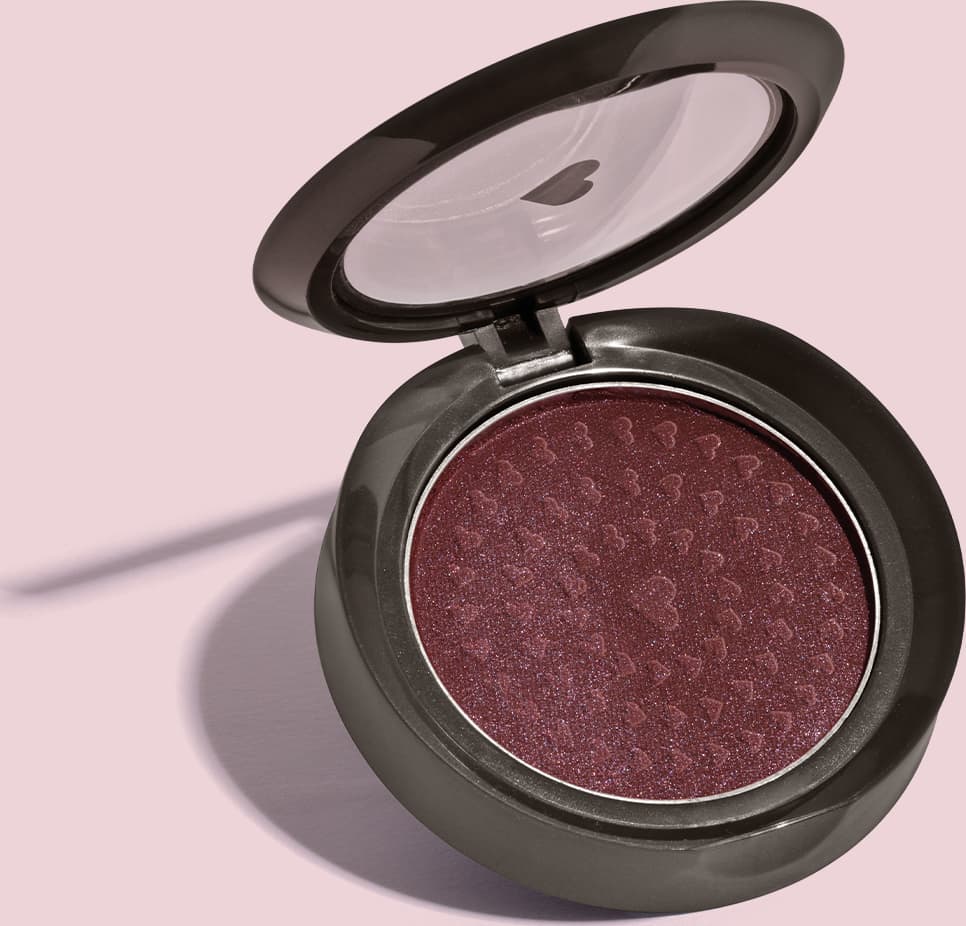Estojo compacto redondo na cor preta com tampa transparente com coração ilustrado contendo 2g de blush em pó compacto Rubor Malva Amoratin da marca Quem Disse, Berenice? em fundo lilás.