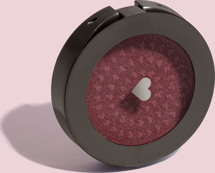 Estojo compacto redondo na cor preta com tampa transparente e coração ilustrado contendo 2g de blush em pó compacto Rubor Cobre Cobrelito da mara Quem Disse, Berenice? em fundo lilás.