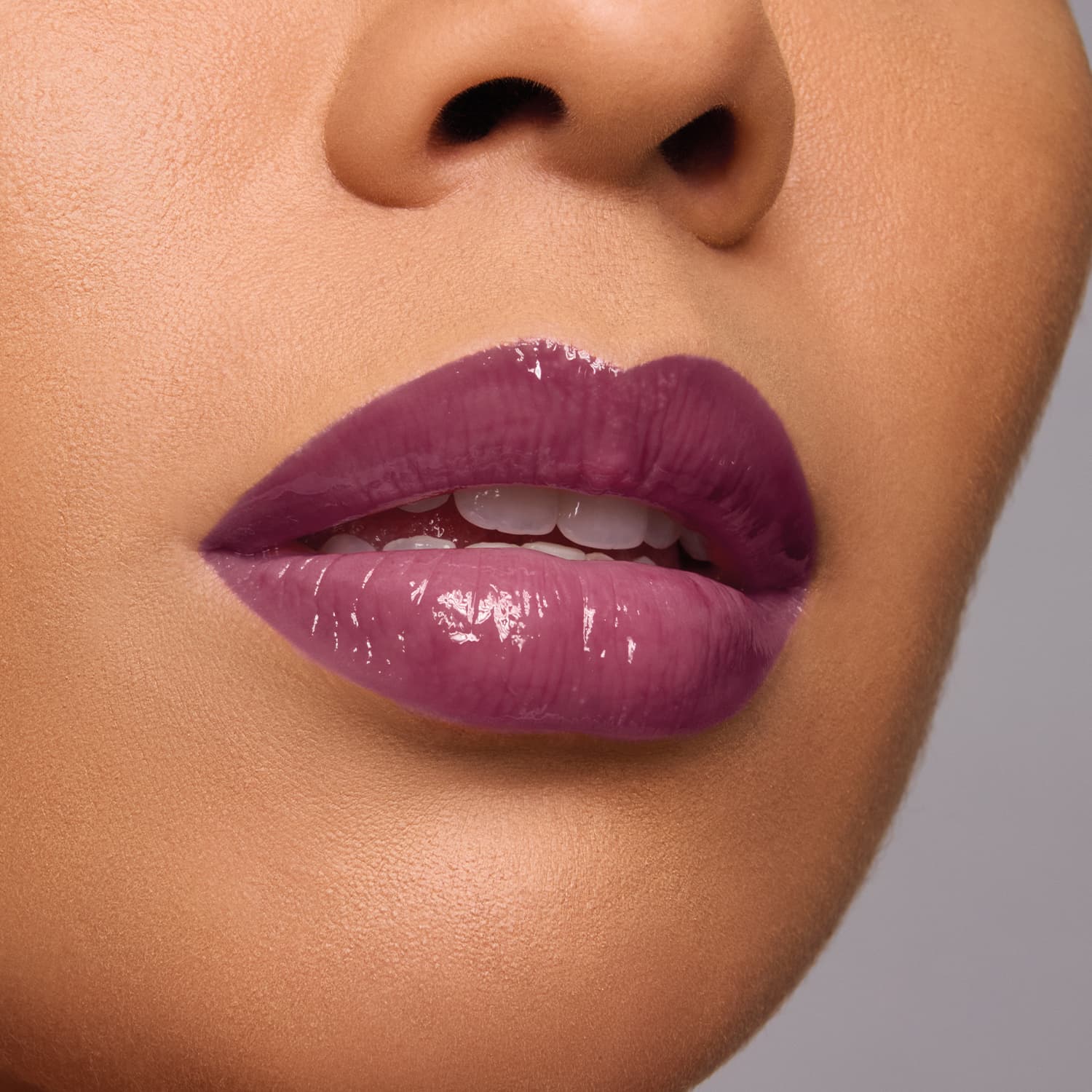 Imagem de um rosto em close-up evidenciando os lábios femininos com batom roxo-rosado brilhante, em primeiro plano contra fundo neutro.