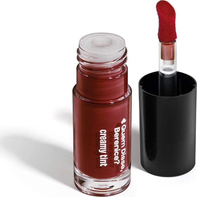 A imagem mostra um recipiente transparente de gloss labial da marca Quem Disse, Berenice? na cor vermelho cereja, com aplicador vermelho, haste transparente, tampa preta. Ele está em uma superfície branca com um leve sombreado.