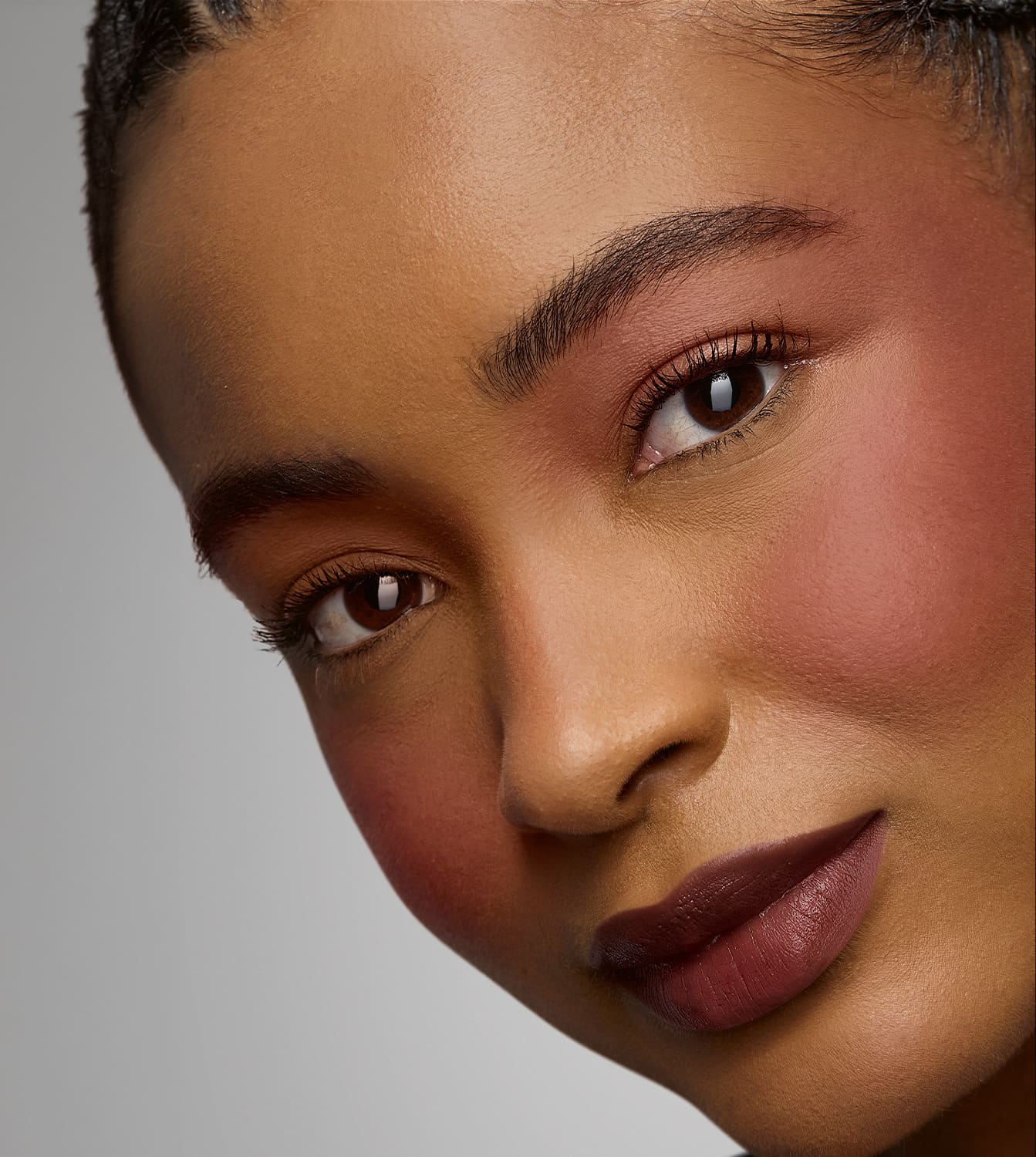 Rosto de uma pessoa com pele negra, olhos expressivos e lábios rosados. Fundo neutro e iluminação suave destacam os traços faciais. A imagem transmite uma sensação de beleza e elegância.
