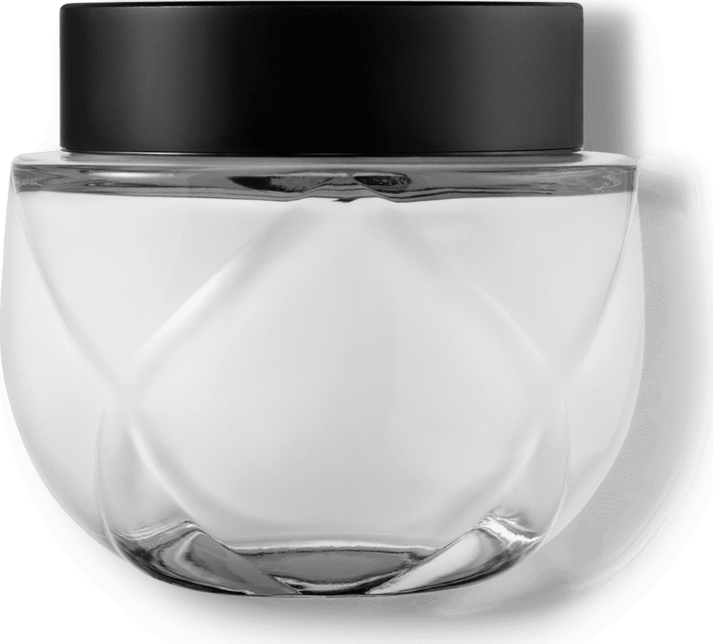 Frasco de vidro transparente arredondado com tampa preta. O recipiente tem uma forma esférica achatada. A tampa preta opaca contrasta com o vidro transparente do frasco que contém o creme na cor branca.