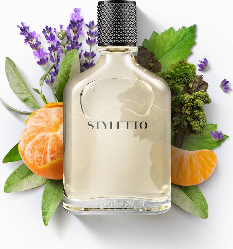 Ambiente de fragrância sofisticado, com flores e folhas verdes, laranja e roxo, destacando a garrafa da marca Styletto em fundo branco. Cenário elegante e natural, sugerindo um produto de beleza de alta qualidade.