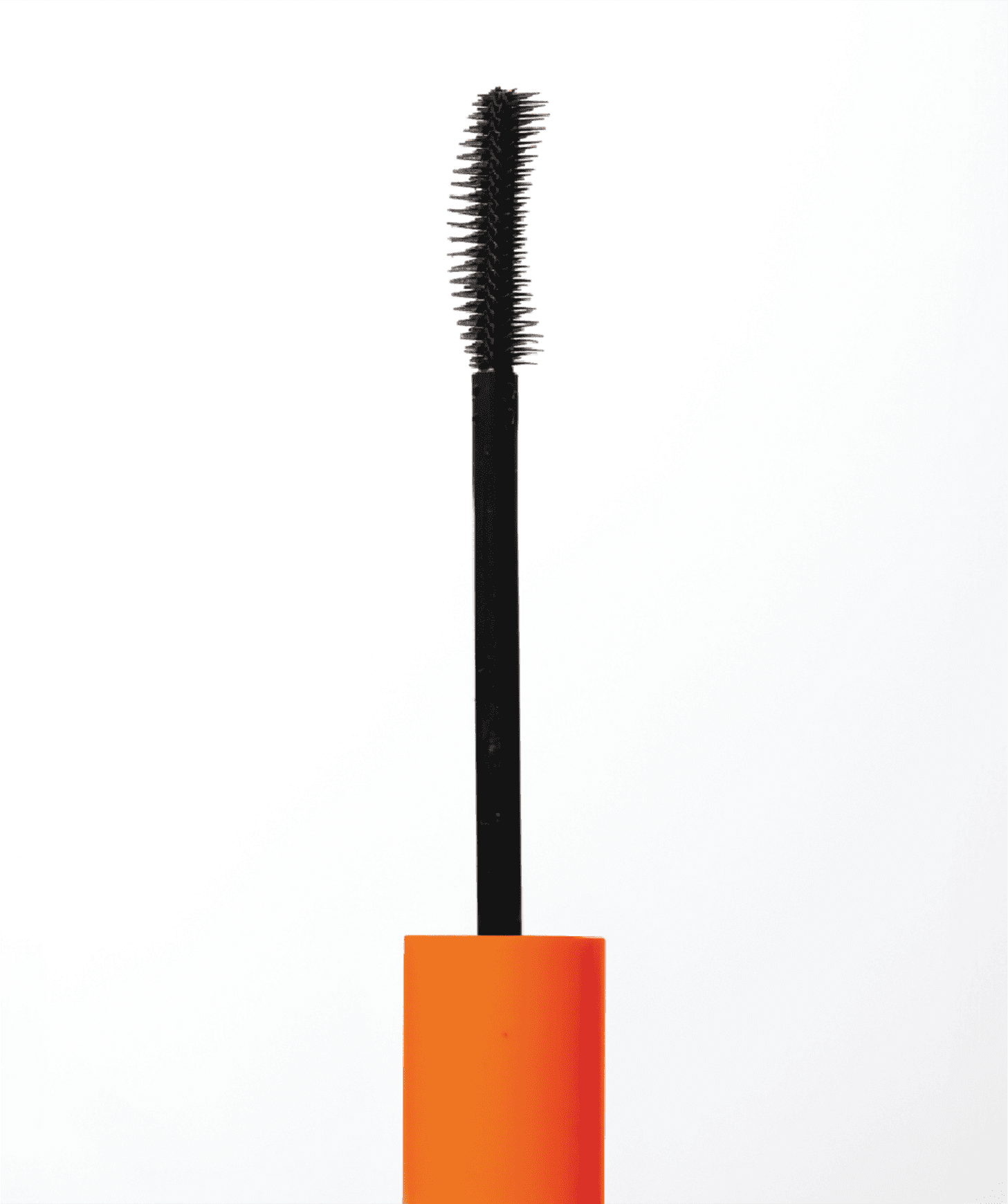 A imagem mostra o pincel para aplicação de máscara para cílios. Cabo plástico na cor laranja e haste metálica com cerdas pretas e longas, formando um pincel espesso e cilíndrico.