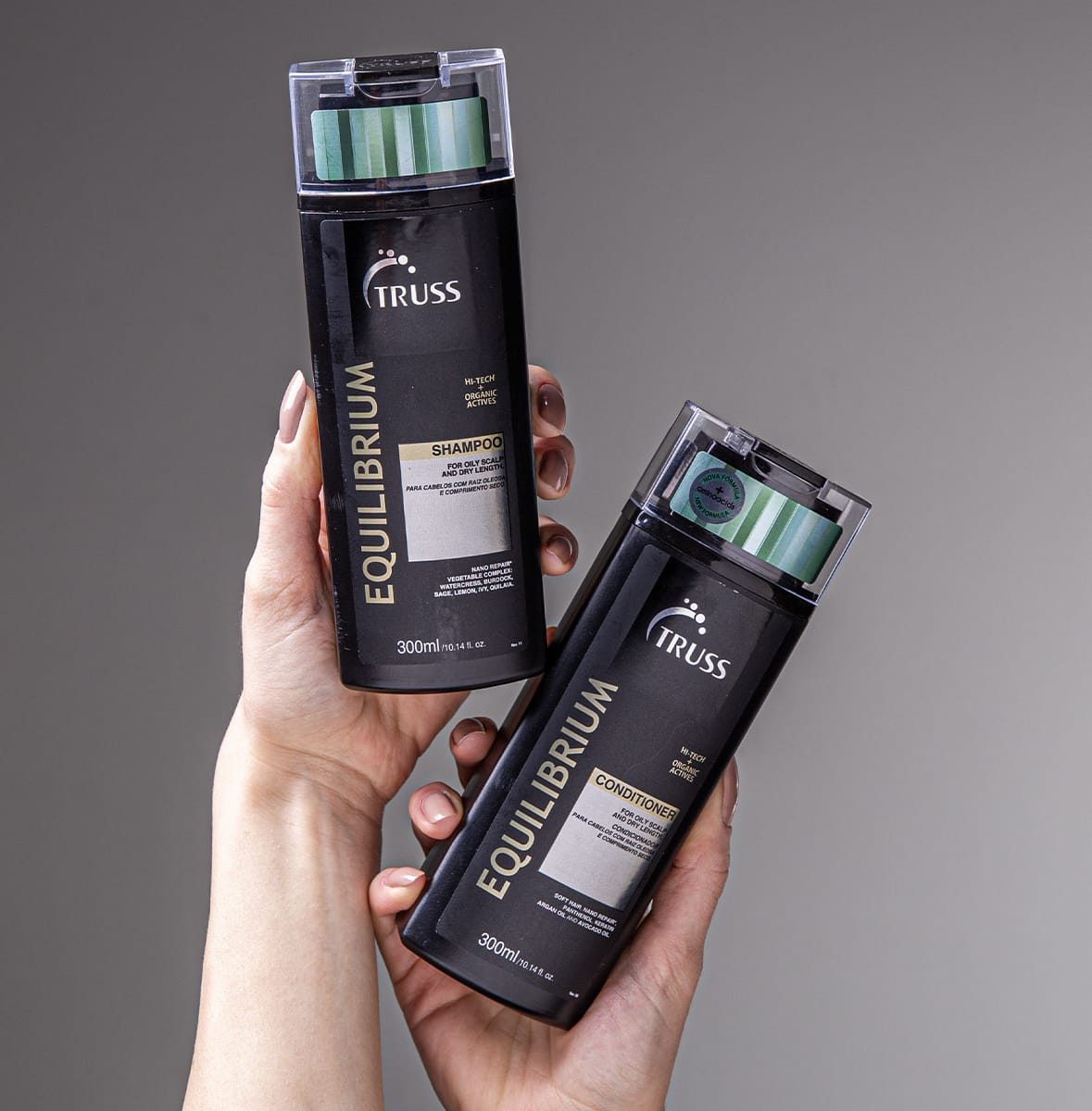 A imagem mostra duas embalagens de produtos para cabelos da marca Truss. Um é um shampoo e o outro é um condicionador, da linha Equilibrium. As embalagens são pretas com detalhes em verde e estão sendo seguradas por uma mão.
