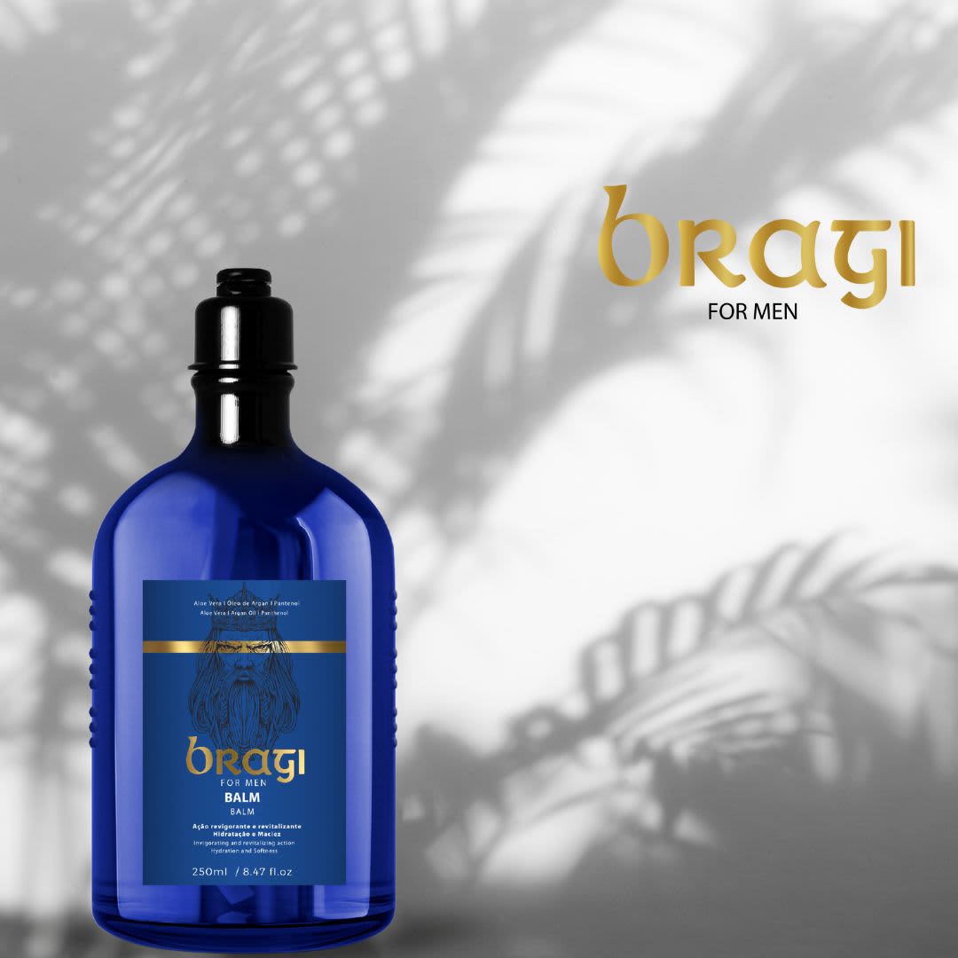 A imagem traz um produto em uma garrafa azul com detalhes dourados e pretos. Ao fundo há uma parede desfocada com sombras de folhas que se parecem com palmeiras.