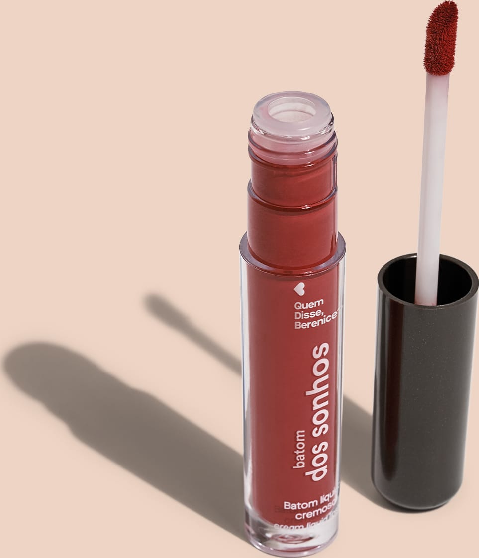 A imagem mostra o frasco do batom labial e ao lado há um aplicador de espuma na cor branca com a ponta no tom marrom e base preta.