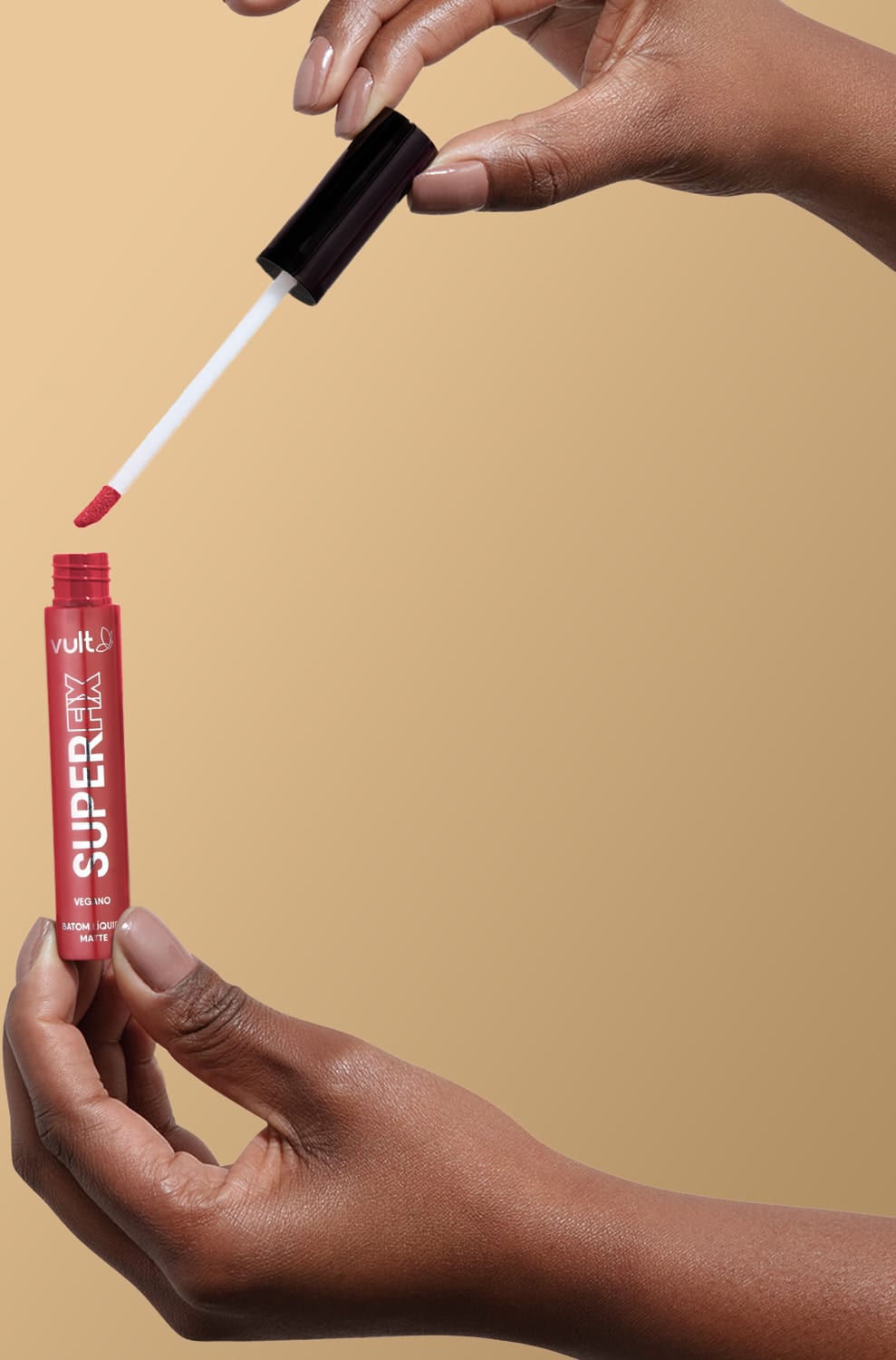 A imagem mostra uma mão segurando o produto aberto do Batom Líquido da marca Vult, na cor vermelha. A embalagem do produto é um tubo vermelho com o nome da marca "Vult" impresso.