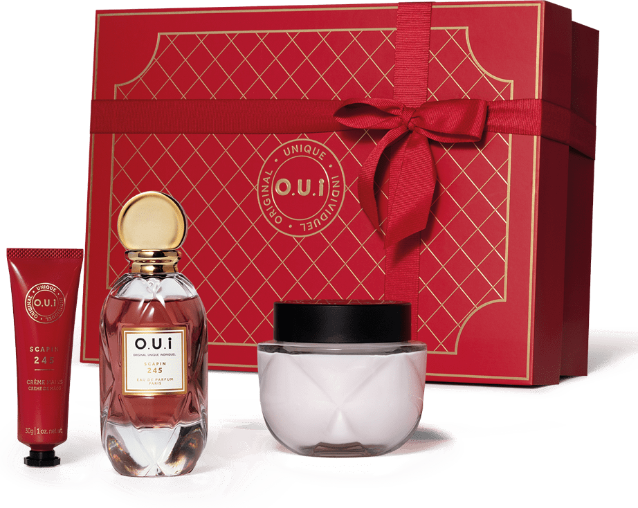 Conjunto. A peça central é o frasco do perfume em vidro transparente com líquido rosa claro e detalhes dourados na tampa e rótulo. Acompanha creme em embalagem redonda de vidro transparente, um frasco tubo vermelho de creme para mãos e caixa de presente