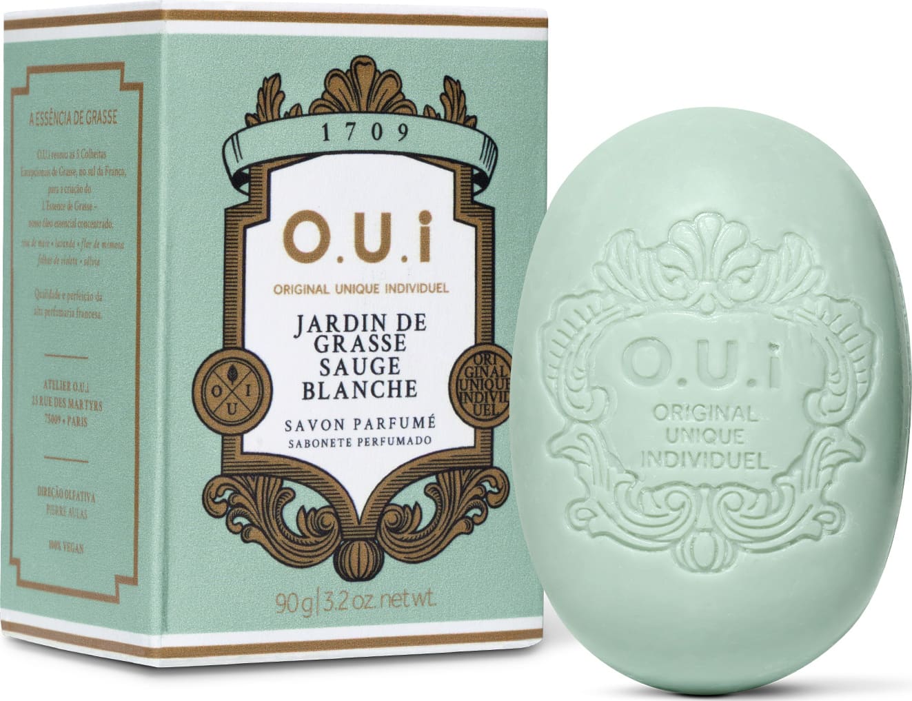 Sabonete perfumado em formato oval com relevo da marca O.U.I. ao lado da embalagem verde-menta com detalhes dourados e rótulo com informações sobre o produto "Jardin de Grasse Sauge Blanche".