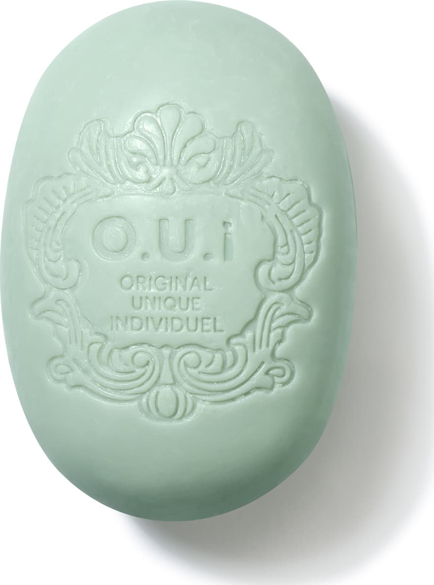 Sabonete em barra de cor verde-clara com textura e design elaborado, com o logotipo e nome da marca "O.U.i. Original Unique Individuel" gravados na superfície.