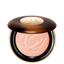 A imagem mostra o sérum iluminador Lancôme. A embalagem é redonda com tampa marrom e logotipo dourado no centro. A parte inferior preta com aro dourado. Interior contém o pó iluminador rosado com padrão rendado.