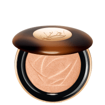 A imagem mostra o sérum iluminador Lancôme. A embalagem é redonda com tampa marrom e logotipo dourado no centro. A parte inferior preta com aro dourado. Interior contém o pó iluminador bege com padrão rendado.