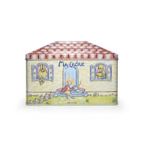 Caixa retangular de metal decorada com ilustrações coloridas. A tampa apresenta um padrão de telhas vermelhas e brancas. Na parte frontal, há uma cena ilustrada com uma figura feminina loira sentada em um banco, segurando um livro, em frente a uma casa.