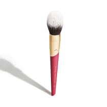 Pincel de maquiagem com cabo rosa e dourado. Parte rosa do cabo tem Niina Secrets impresso em dourado. A parte superior é dourada. O pincel tem cerdas brancas e marrons, formando uma cabeça arredondada e densa.