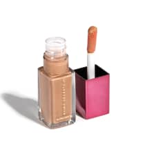 Frasco de cristal com gloss labial dourado da marca Niina Secrets, embalado em frasco de vidro, quadrado, transparente com tampa rosa. O produto apresenta um aplicador de espuma na ponta.