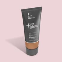 O produto apresentado é uma base líquida da marca Tô no Glow, com embalagem em tubo plástico preto e branco. O rótulo exibe o nome da marca e a descrição "Radiância natural, leveza e conforto". O produto é classificado como "Base líquida".