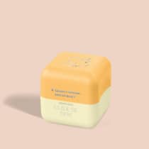 Balm Labial em formato hexagonal, com duas seções de cores distintas de amarelo. A parte superior é amarela com um desenho estilizado de uma abelha. Há um texto em português que diz "Quem disse, Berenice?" e "Oboticario CUIDE-SE BEM".