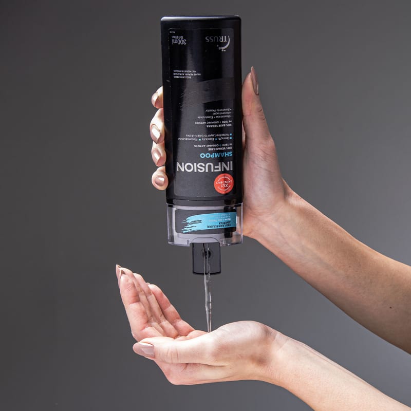 A imagem mostra o shampoo Infusion sendo segurado por uma mão e dispensado em uma mão aberta.