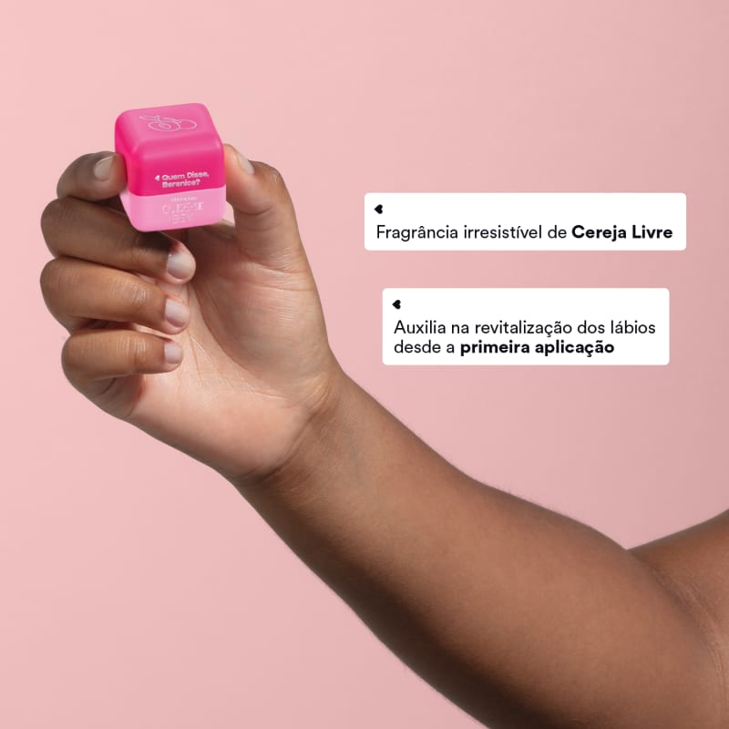 O produto é um hidratante labial da marca Quem Disse, Berenice?. A embalagem é um pequeno tubo plástico rosa vibrante com o logotipo da marca impresso. O produto está sendo segurado por uma mão.