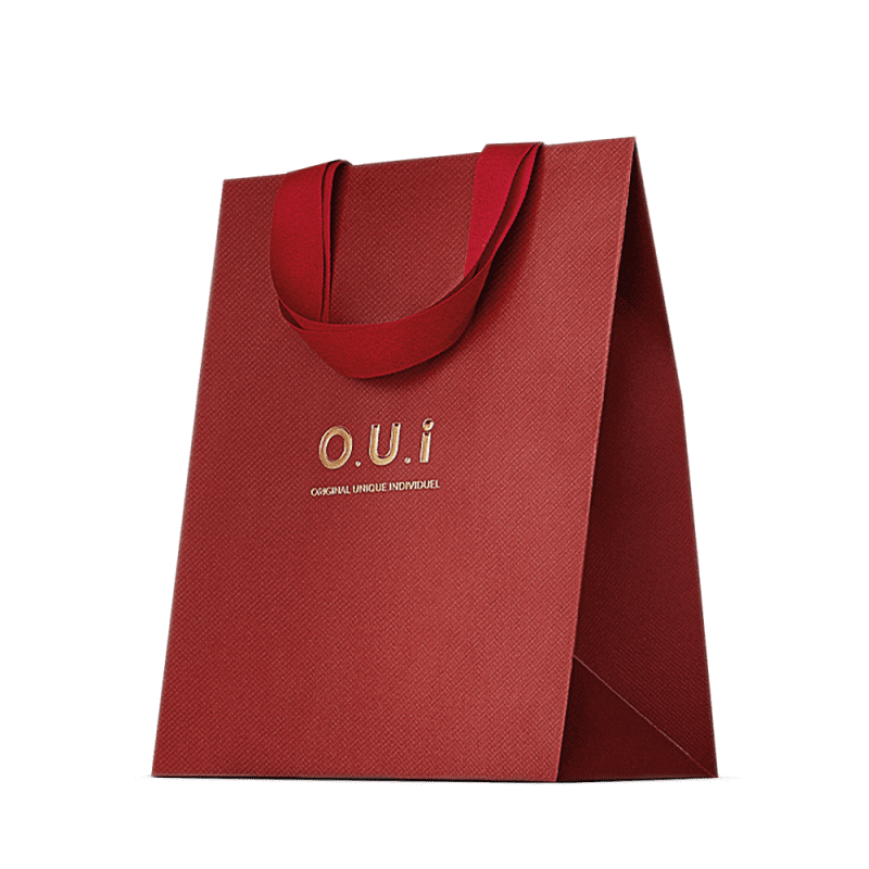 Sacola de presente vermelha em material texturizado, com alças e detalhes na mesma cor. Apresenta o logotipo "O.U.i" em letras douradas. A embalagem tem um design minimalista e elegante, com o vermelho vibrante como cor predominante.