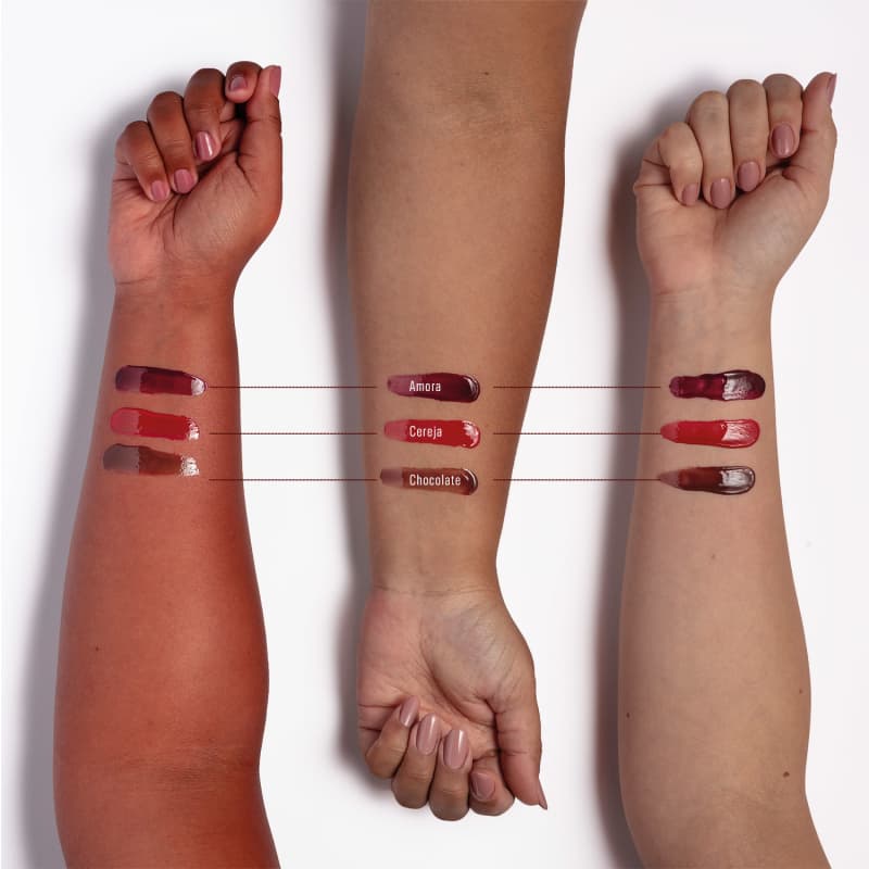 Imagem de braços com aplicação do Hidratante Labial, nas cores Amora em diferentes tons de pele. Em pele avermelhada os tons ficam brilhantes e com menor contraste; em pele parda, ficam com brilho médio, na pele branca, ficam nítidos e vibrantes.