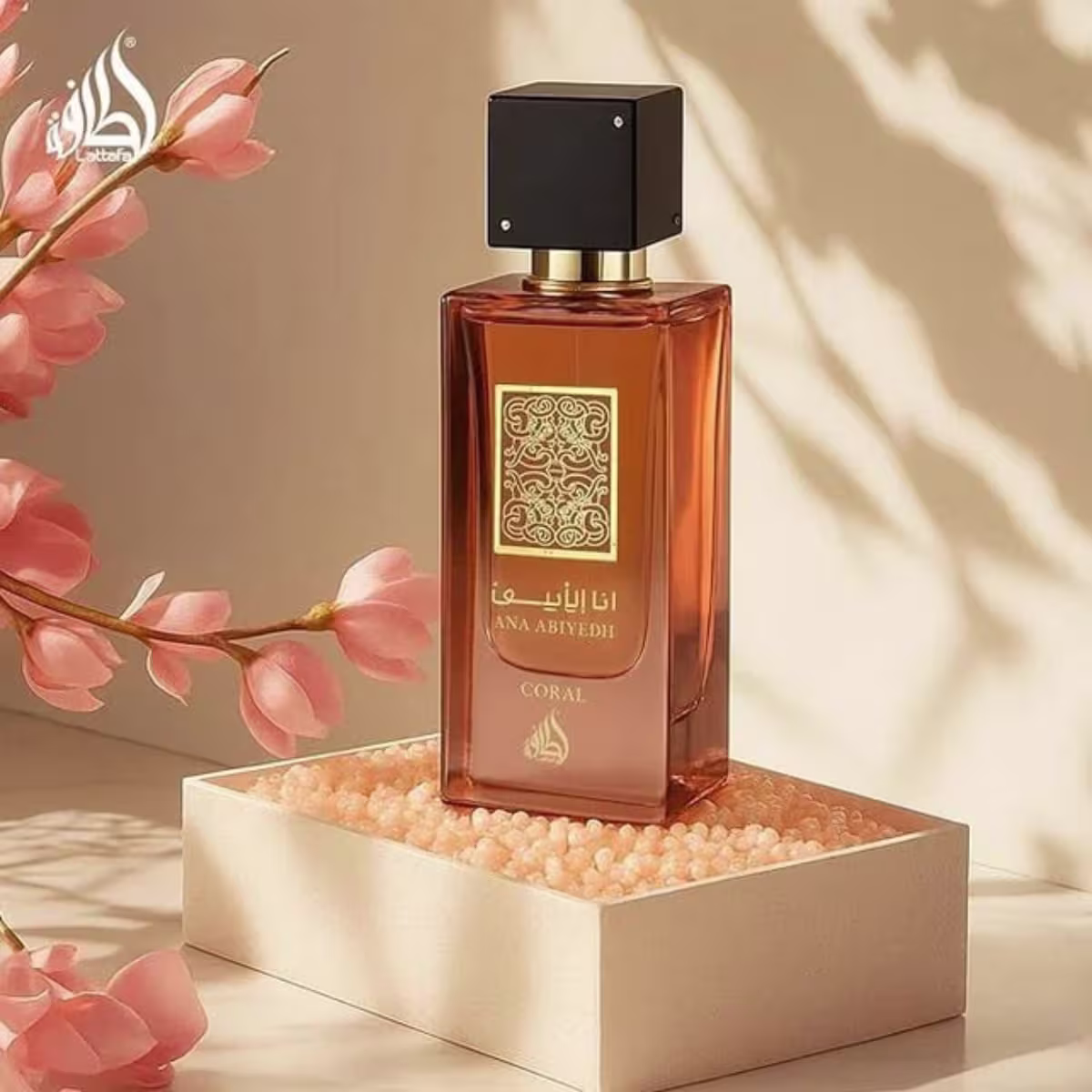 Ambiente elegante e sofisticado com flores de cor coral, caixa dourada e frasco de perfume da marca Lattafa Perfumes, destacando a fragrância em um cenário iluminado e harmonioso.