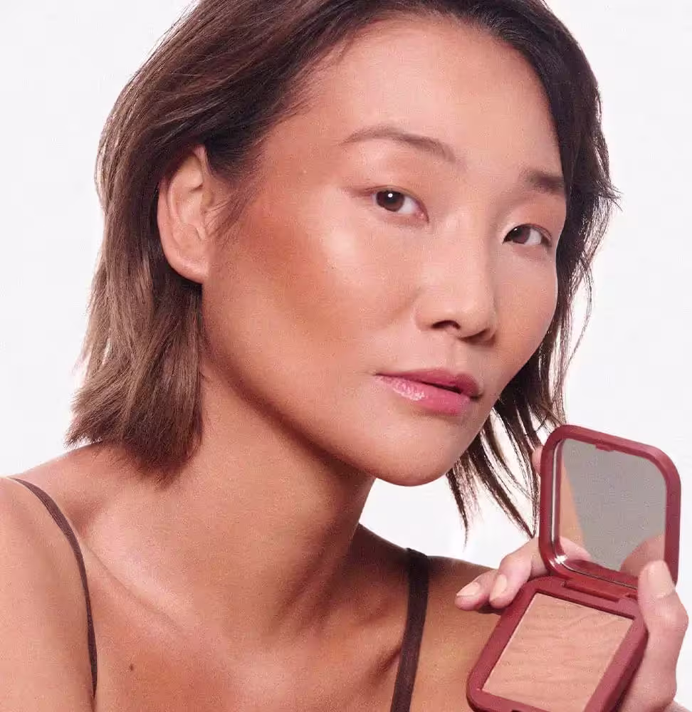 A imagem mostra uma mulher segurando o Bronzer Mascavo Summer Glow e destaca o efeito bronzeado da maquiagem