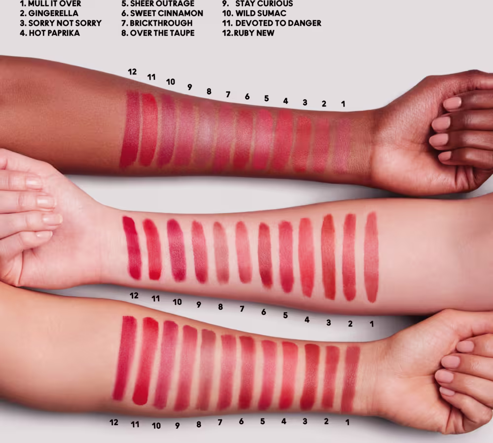 A imagem mostra 3 antebraços com as amostras de todas as cores de batons da linha, com indicações numéricas e as legendas acima. Um braço é negro e os outros dois são brancos, indicando como cada cor fica em tom de pele específico.