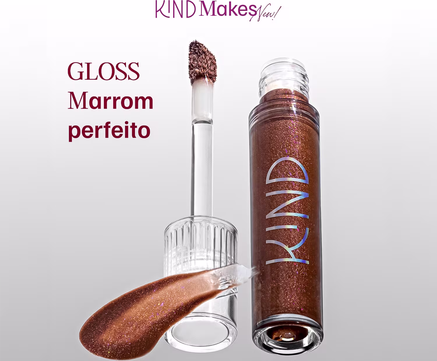 A imagem mostra a tampa da embalagem do gloss com o aplicador virado pra cima, semelhante a uma tampa de batom, transparente, cilíndrica, com uma amostra de cor. Ao lado, o frasco do gloss, com o produto de cor marrom e palavra KIND escrito na embalagem.