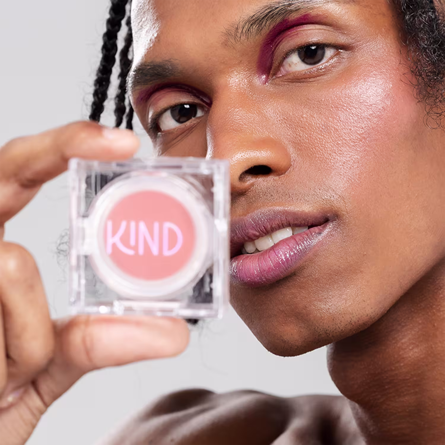 A imagem mostra um homem negro segurando a embalagem fechada do blush com os dedos, polegar e indicador, ao lado do seu rosto.