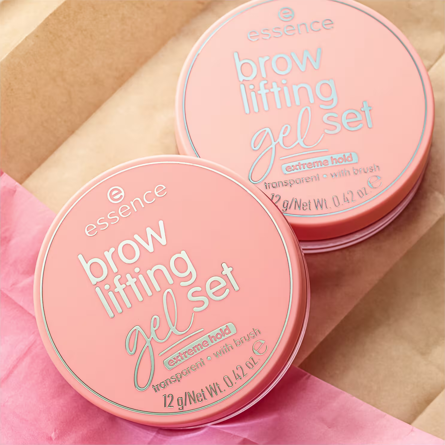 A imagem mostra duas embalagens do gel para sobrancelhas.  São dois potes redondos em tons de rosa coral, que trazem as informações do produto destacada nas tampas em um tom prata metálico.