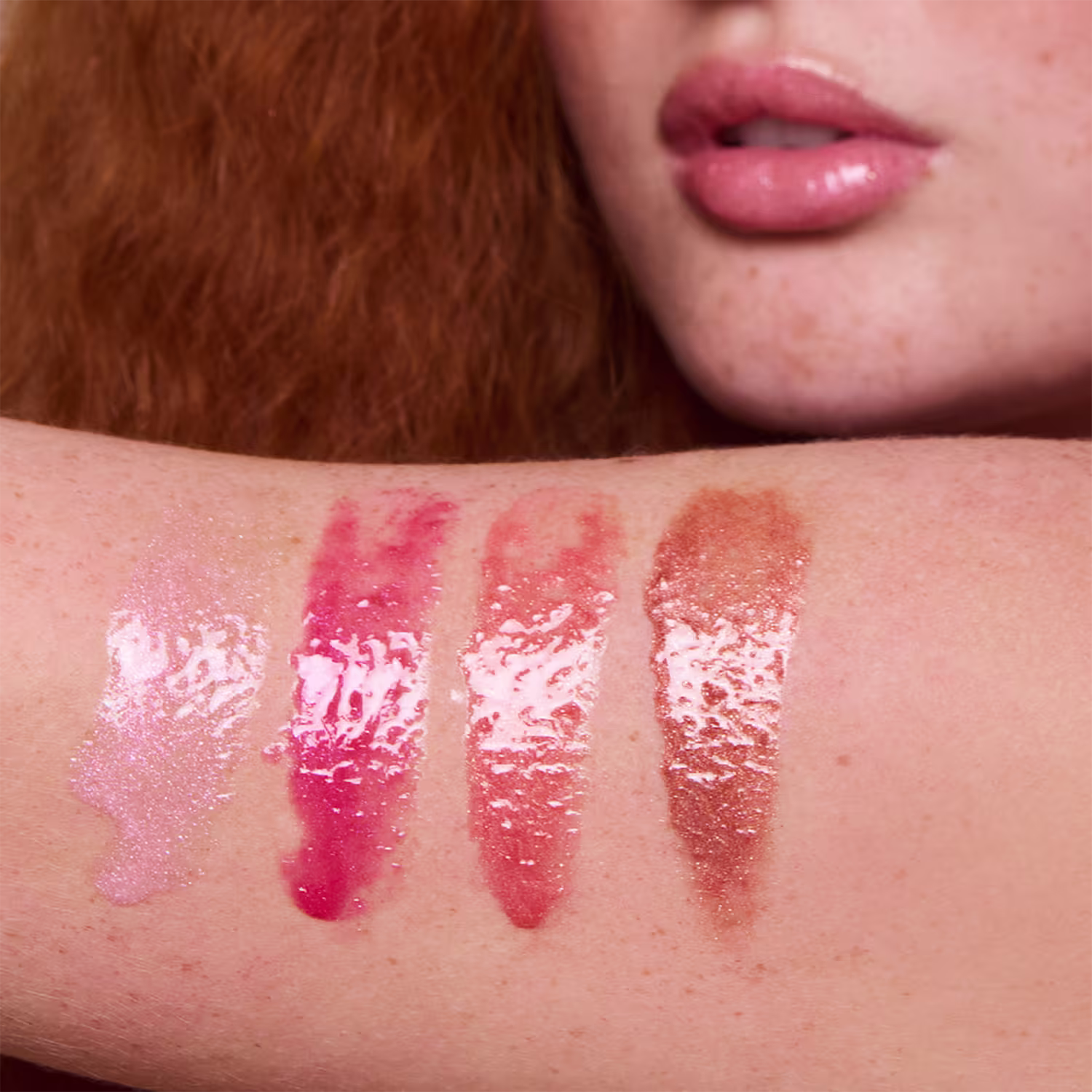 A imagem apresenta amostras das cores do gloss labial de Pam! by Pamella, em um braço branco com sardas. As cores são rosa claro, rosa intenso, pêssego e marrom claro. Apresentam um brilho perolado bem vivo.