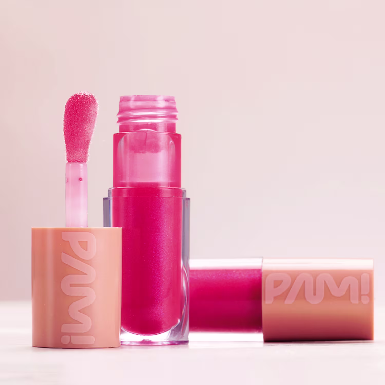 A imagem apresenta duas embalagens do gloss de PAM! by Pamella. Uma está na vertical com o aplicador ao seu lado e outra está atrás na horizontal.