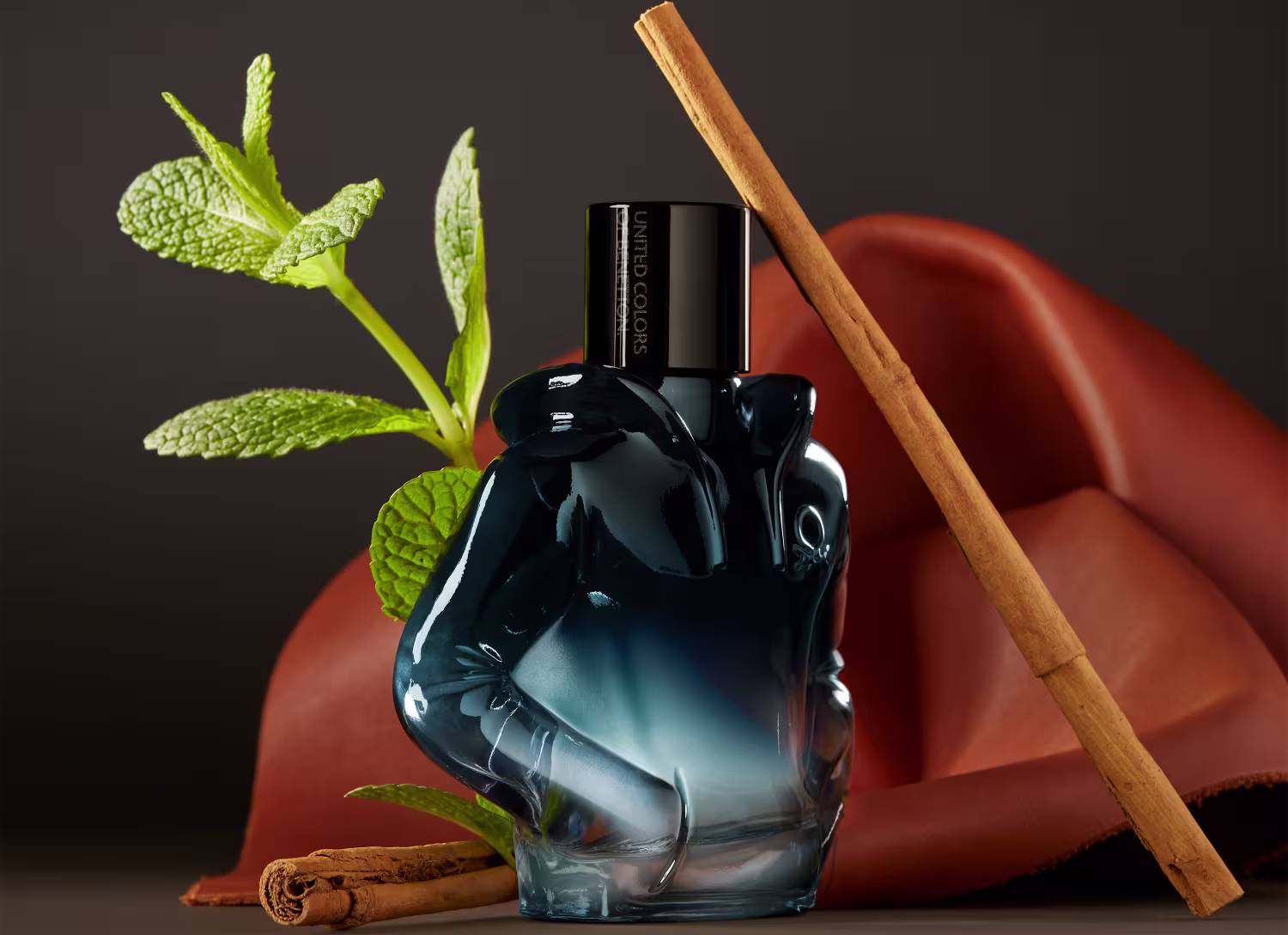 Frasco do perfume em um cenário com fundo marrom, há um pau de canela e um ramo de hortelã ao redor.