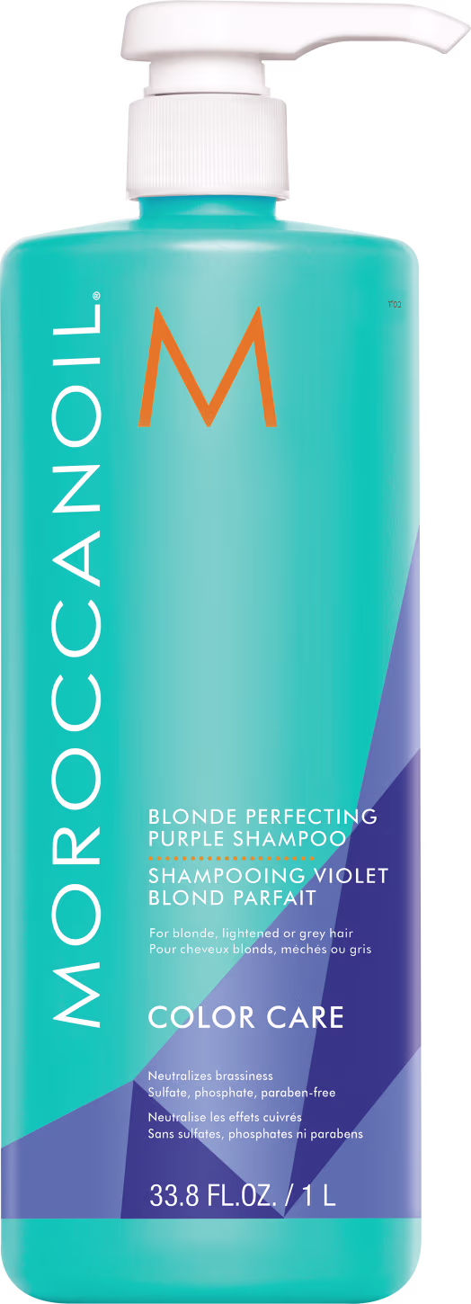A imagem mostra o Shampoo Moroccanoil Color Care Blonde Perfecting 1L, um frasco cilíndrico azul claro com detalhes em roxo e laranja e aplicador pump branco. De acordo com as informações na embalagem, tem a função de neutralizar os tons amarelados.