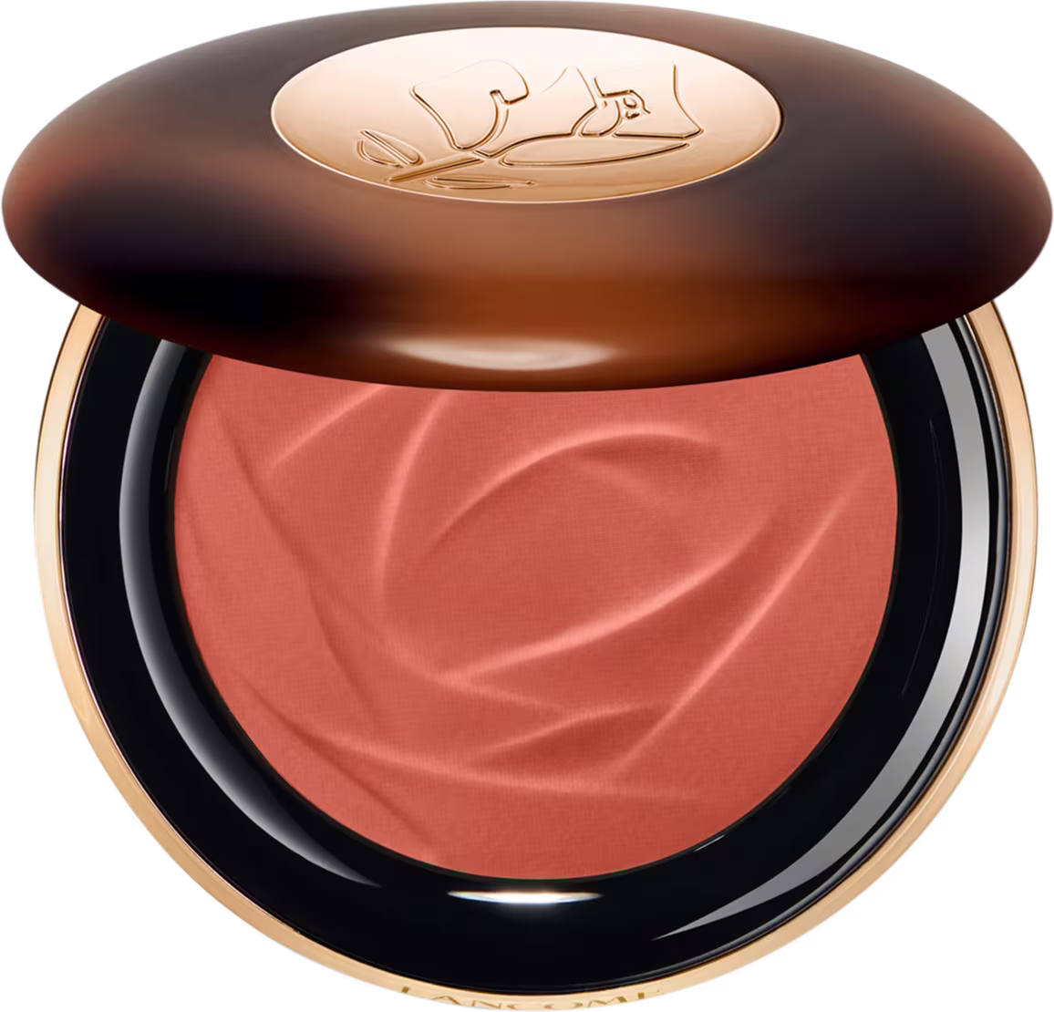 A imagem traz um sérum bronzeador compacto em uma embalagem. A tampa superior é marrom com alguns detalhes mais claros e tons mais escuros. O logotipo da marca aparece gravado em dourado no centro da tampa e o produto possui uma cor rosada.