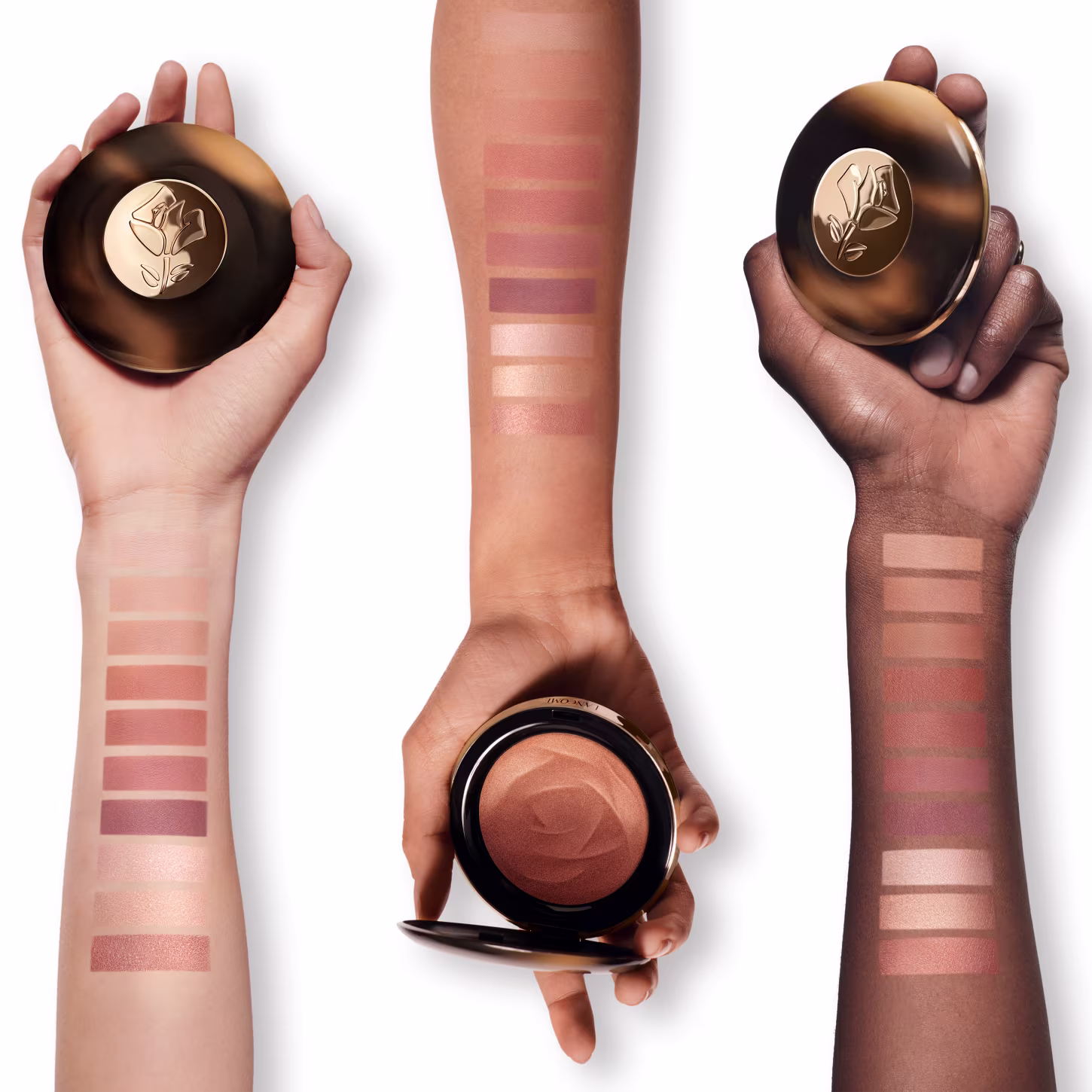 A imagem trás três embalagens com o bronzer. Elas têm formatos cilíndricos e são segurados por mãos femininas de diferentes tons de pele. No antebraço estão as tonalidades do bronzer e como eles ficam em cada pele.