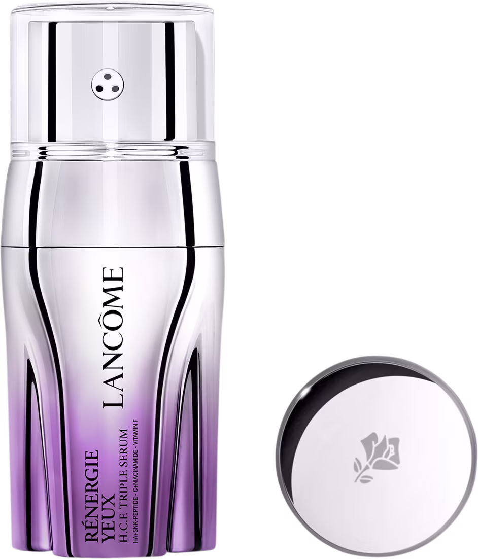 Sérum em frasco cilíndrico com degradê de roxo na base. O frasco tem tampa prateada com pequeno orifício central. Ao lado, tampa prateada redonda com logotipo floral gravado. Embalagem minimalista com nome do produto e marca visíveis no frasco.