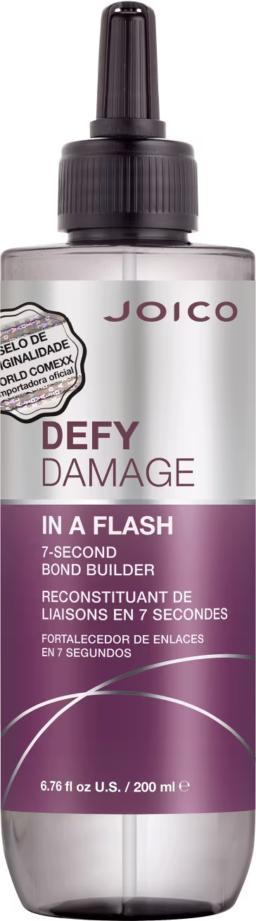 É um produto de tratamento capilar da marca Joico. A embalagem é um frasco que tem um aplicador preto na parte superior. O rótulo na frente é predominantemente branco e roxo. O nome do produto "Defy Damage In a Flash" está escrito em letras grandes;