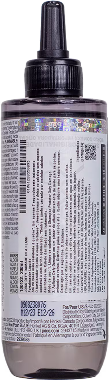 Imagem mostra o verso do produto com rótulo branco com texto informando código de barras e informações do produto visíveis no rótulo. Formato cilíndrico alongado típico de embalagens de produtos capilares líquidos.