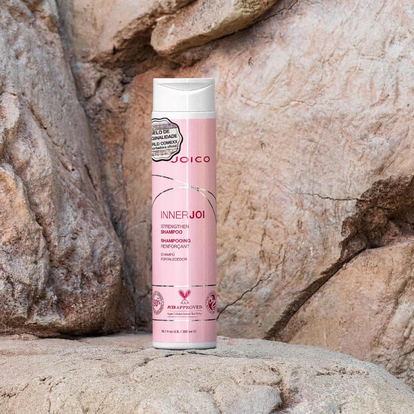 No centro, o Shampoo Joico InnerJoi Strengthen (300ml) destaca-se em sua embalagem laranja claro com detalhes em branco e prata. No fundo, imagem da natureza com rochas.