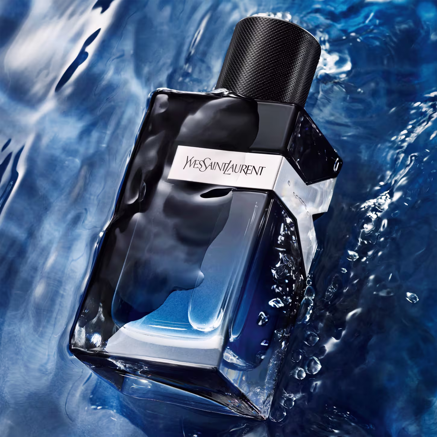 A imagem mostra o frasco do perfume em uma superfície aquosa azul escura. Ele está molhado, evidenciando o frescor da fragrância.