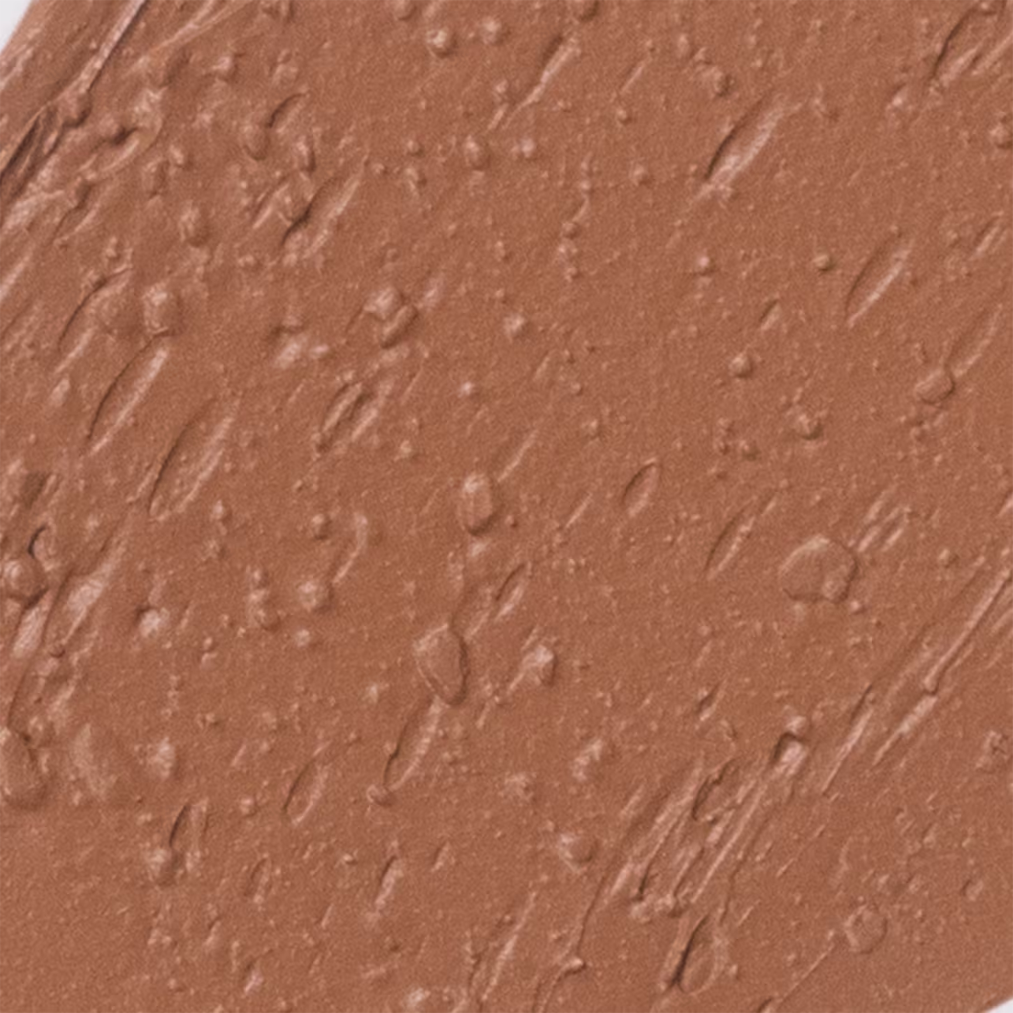 A imagem apresenta detalha da textura da base Océane Edition Foundation Stick. A superfície apresenta uma tonalidade marrom e textura em bastão cremosa.