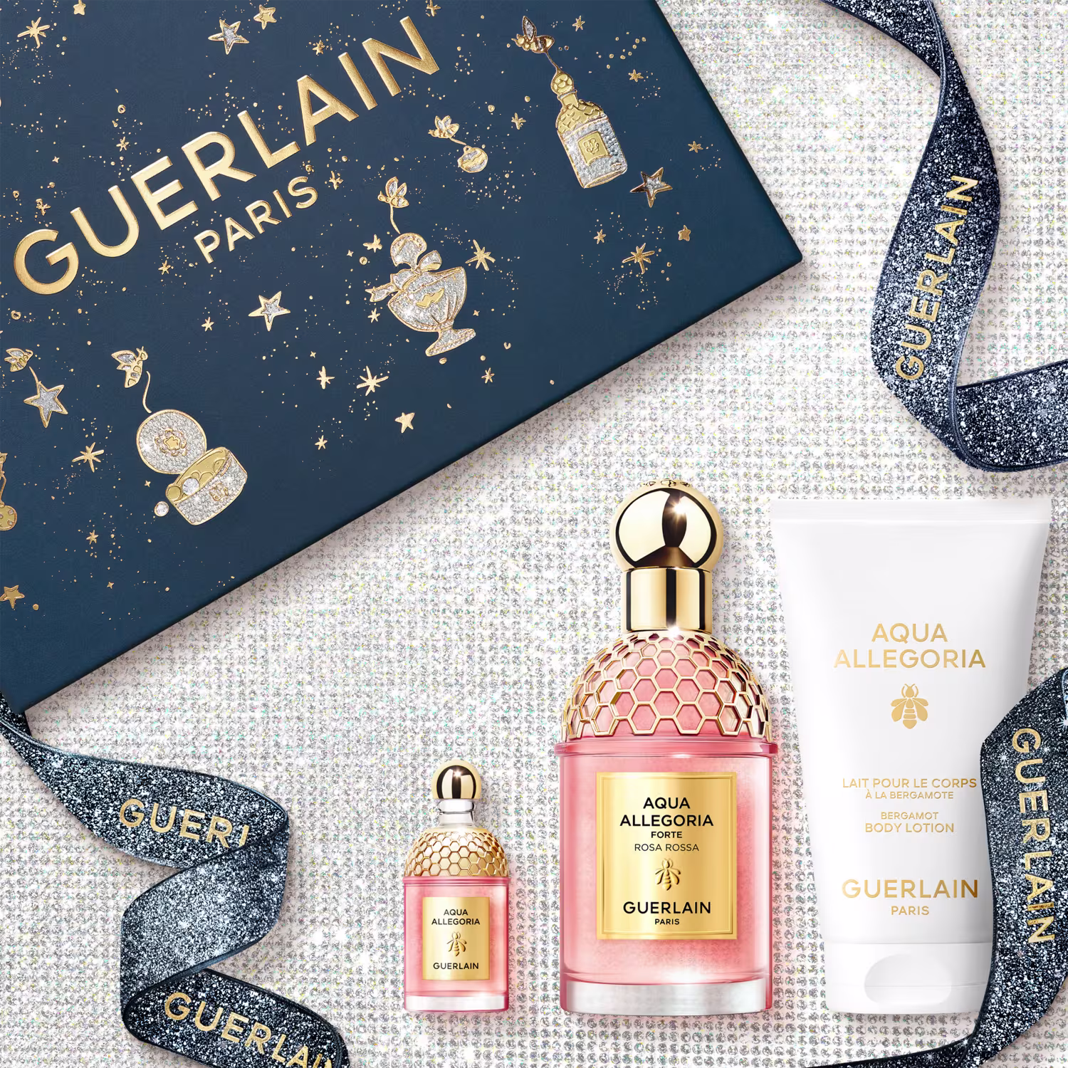 A imagem mostra um kit com perfume, versão travel size e body lotion. Os perfumes em frascos rosa com detalhes e tampas dourados, e o body lotion com embalagem branca. Acompanha uma caixa presenteável azul.