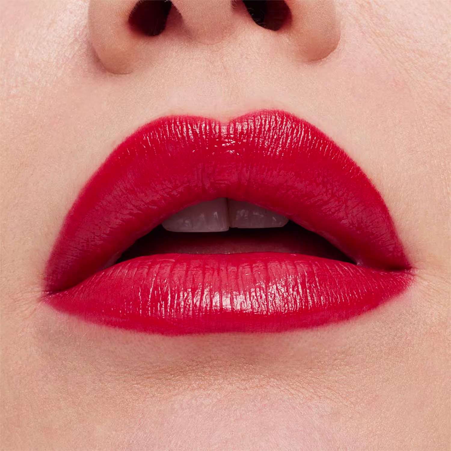 O produto é um batom de cor vermelha vibrante e acabamento cremoso. Apresenta uma textura aveludada e cobertura opaca intensa. A imagem mostra um close-up de lábios femininos maquiados com esse batom vermelho vivo, ressaltando a pigmentação rica.