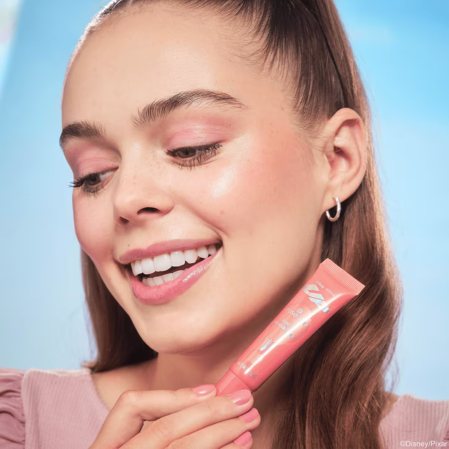 Modelo usando e segurando o Blush Líquido Essence Disney Pixar Up 02 Sunset Serenade 13,5ml.