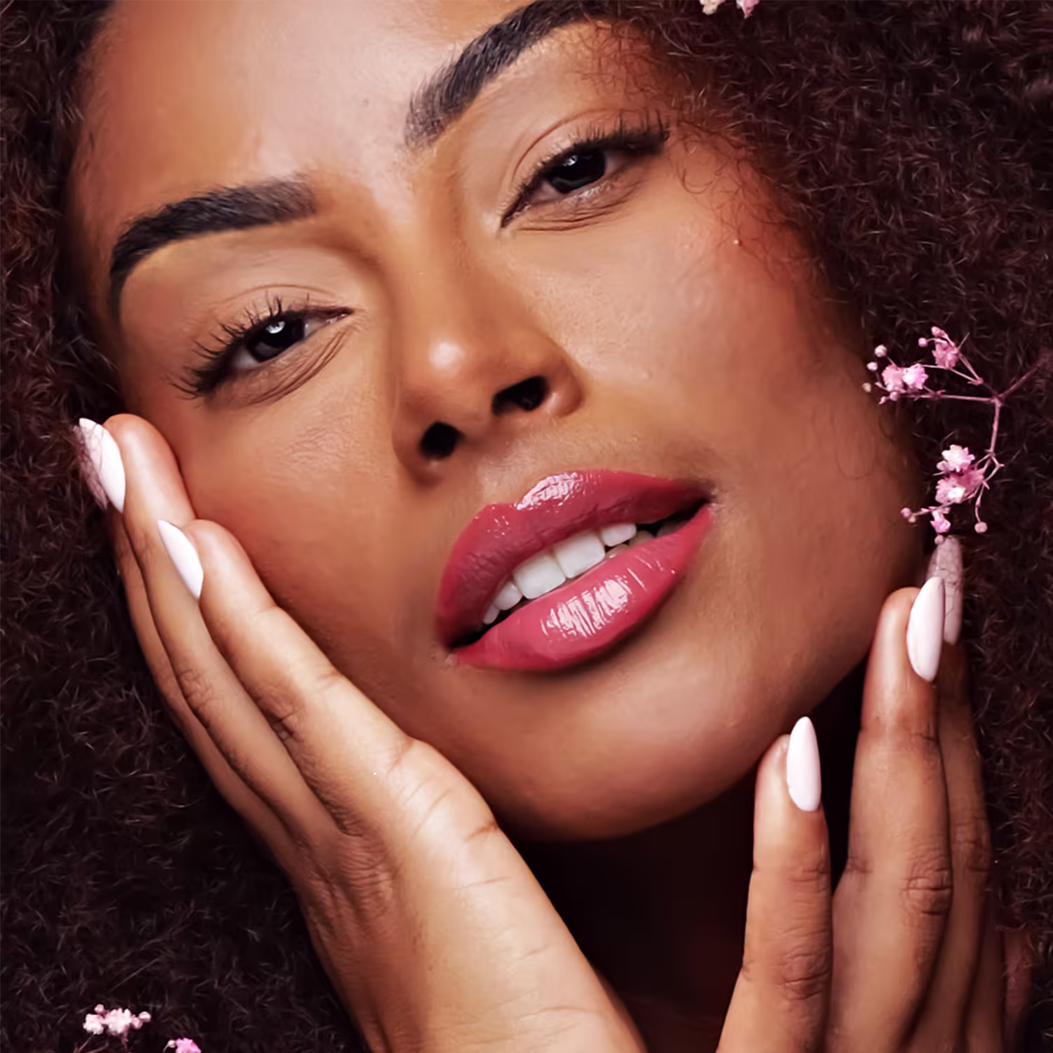 Ambiente de beleza com modelo feminina de pele negra, cabelos cacheados e maquiagem destacada, sugerindo o uso de produtos da marca Fran by Franciny Ehlke. Predominância de tons quentes e florais.